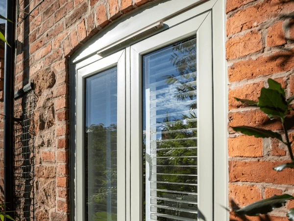 An arched top UPVC window with an opening vent and internal blinds. Above is a central trickle vent