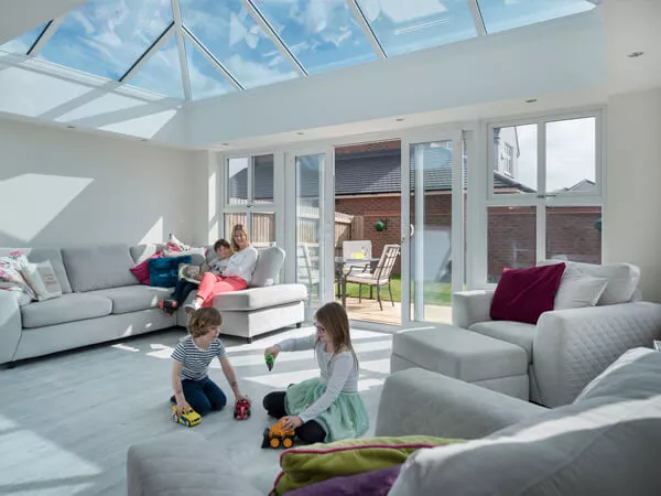 Lady with 3 children in bright orangery with white roof rafters, 4 pain patio doors and windows