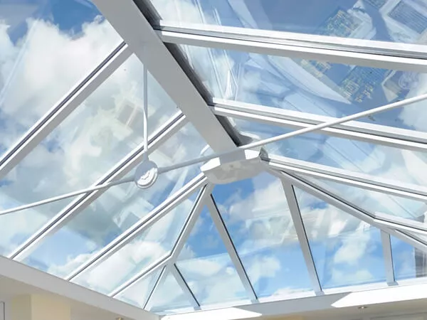 Looking up through a new white UPVC Ultraframe conservatory glass roof towards a cloudy blue sky, the roof has a three way tie bar.