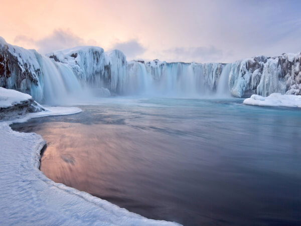 A frozen waterfall and a freezing lake under a cold grey sky.